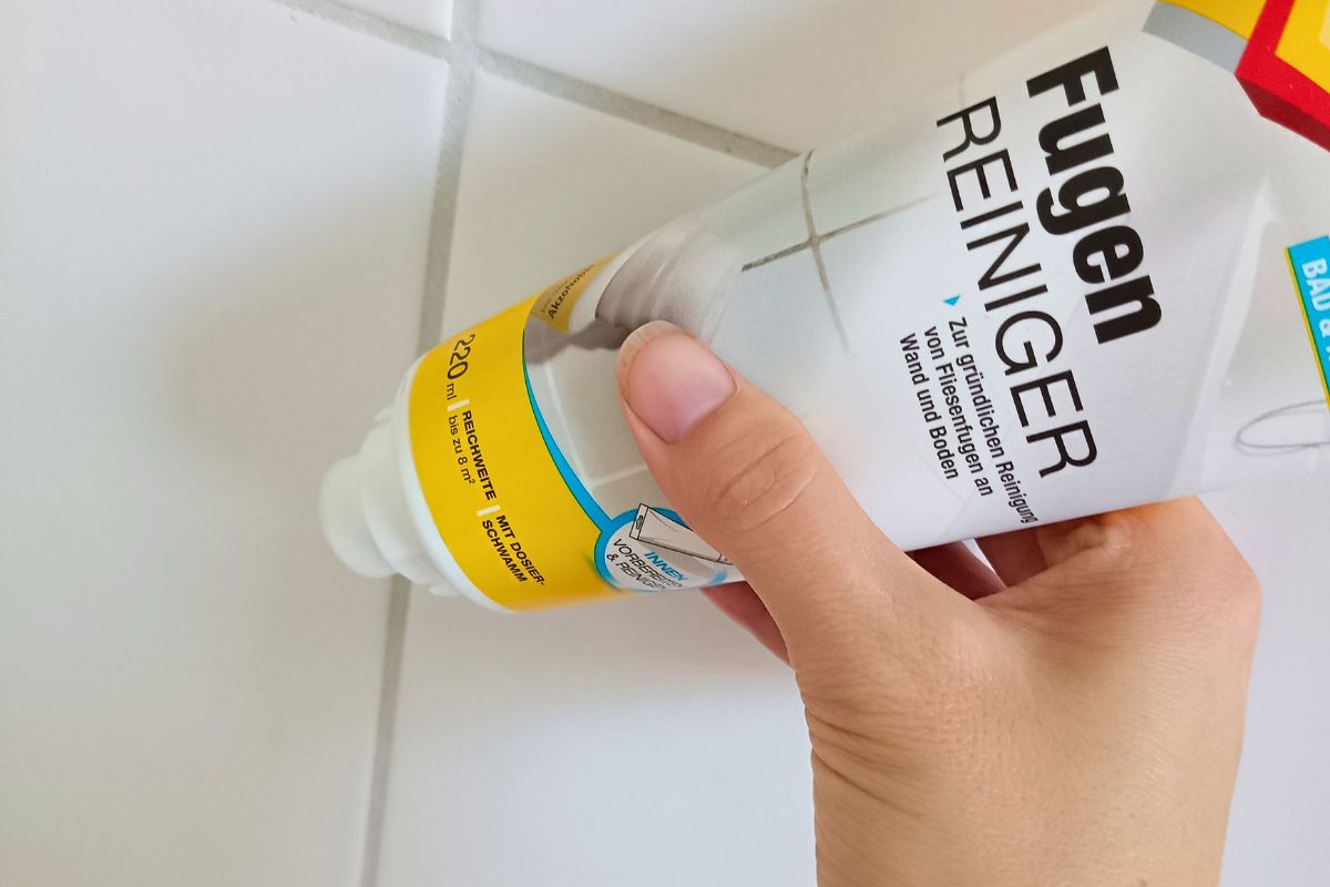 Hand hält Molto Fugenreiniger vor weißer Fliesenwand mit Fugen